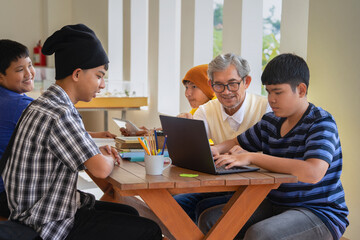 Fototapeta premium math teacher teaching group of teens students to do bar graphs, create illustrated bar graphs on computer laptop, older adult teacher helping four teenage boys to work school project