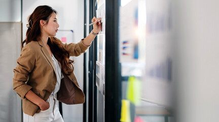 Confident businesswoman standing at office, working on business graph chat on glass wall, planning for new business project finance investment.