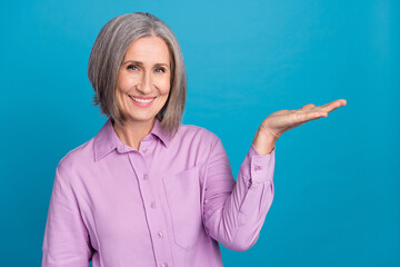 Fototapeta premium Photo portrait of positive satisfied old business woman wear purple formal shirt hold arm demonstrate object promo isolated on blue color background