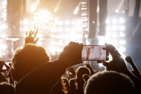 Hand with a smartphone record live music festival and taking photos of the concert.