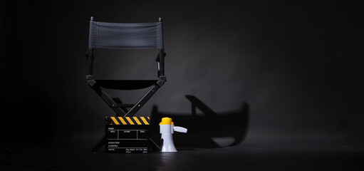 Back of black director chair and yellow clapper board with megaphone on black background. - obrazy, fototapety, plakaty