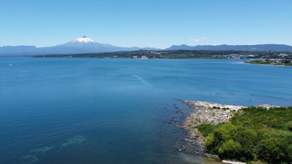 Aerial view of the volcano and mountains, on the shore of a lake in summer, with the city in the distance.