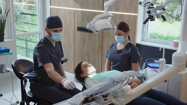 In light clinic assistants and man dentist in medical masks hold dental instrument that treats teeth. Hydience and healthy
