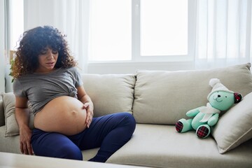 Pregnant woman sitting on the couch lower back pain and headache, strain on the spine during pregnancy. Lifestyle difficulties of motherhood preparation for childbirth, the last month of pregnancy