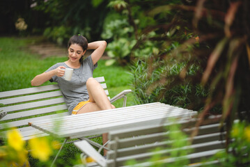 Relaxed young female smiling and looking side, sitting on home terrace. Hobby and resting leisure concept, Gardener girl relaxing after taking care of a plants in home garden. relaxation wellness