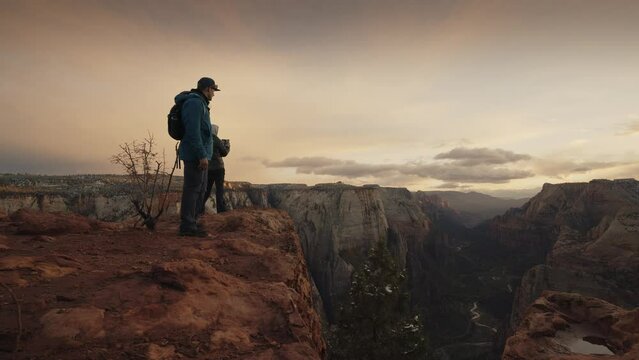 Hikers standing at the edge of Zion Canyon at sunset / Springdale, Utah, United States