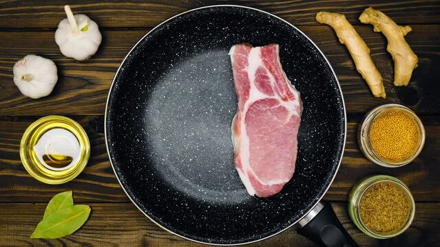 The cook puts the meat on the pan. Frying pan with meat steak, fresh garlic, olive oil, bay leaf, ginger, mustard peas, cumin on a table with a brown background with a wooden texture. Top view. Food