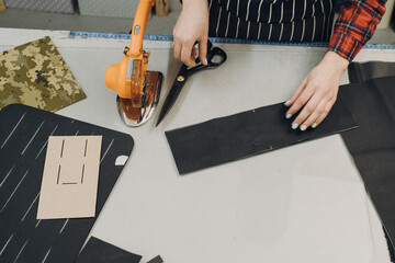 Seamstress at work. Dressmaker cutting fabric. Woman standing at table with cut textile and working on a design. Top view, closeup with copy space. Disc cutting knife