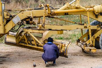 Worker doing adjustments of the motor grader at construction site - obrazy, fototapety, plakaty