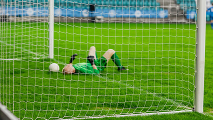 Soccer Football Championship Match: Goalkeeper Loses the Ball in a Goal and Lays on the Grass. Live Sport Channel Broadcast Television Concept. Stylish, Through Goals Net Shot.