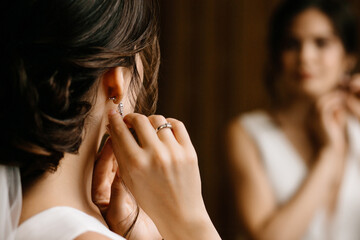 the bride adjusts her earrings close-up with reflection in the mirror