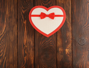 Gift box in the shape of a heart with a bow on a wooden textured background, top view