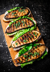 Sandwich with grilled eggplant and lettuce on a wooden cutting board. 