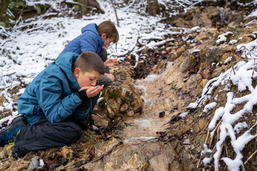 Children drinks mineral water from natural spring. The concept of travel to the wild in the winter