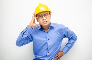 asian male construction worker or engineer in blue shirt and safety yellow helmet shows expresion of anger, furious and dissapointment isolated over white. stressed over work concept