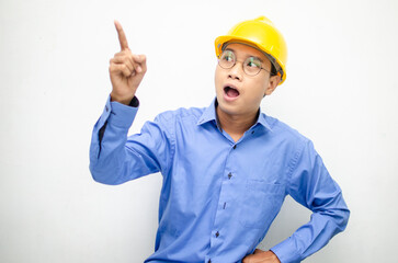 A happy, shocked asian consrtuction worker in blue shirt and yellow safety helmet pointing finger and presenting something ads. 