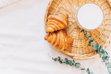 Wicker tray with croissants and coffee on white bed linen.