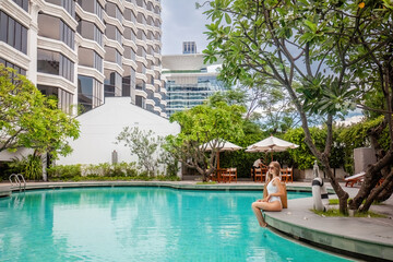 Woman on summer vacation, sitting on edge of hotel swimming pool