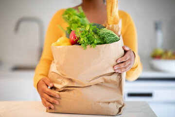 Millennial african american woman in casual unbaking paper bag with organic vegetables