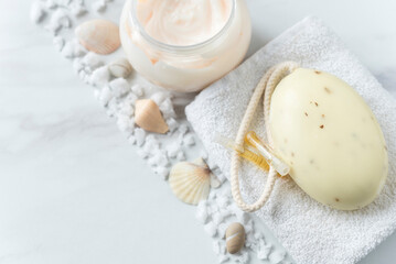 Fototapeta na wymiar Spa composition of soap, towel, skin cream, vial of oil, scattered sea salt and shells. Flat lay. Top view. Copy space