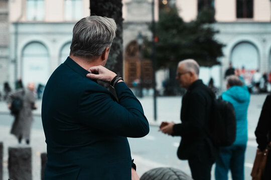 Unrecognizable elegant man adjusts his jacket collar. A man with white hair waits for customers at the entrance to a rich restaurant. Urban lifestyle.
