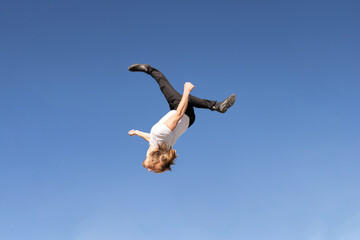 caucasian blond boy doing a backflip and parkour with blue sky in the background