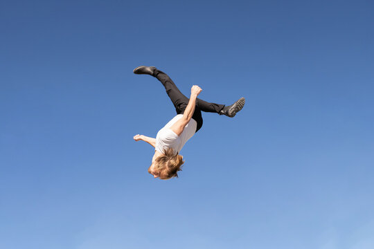 caucasian blond boy doing a backflip and parkour with blue sky in the background