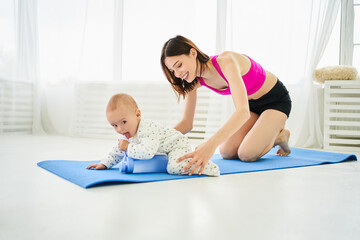 Young mother having fun with her baby at home on a yoga mat.