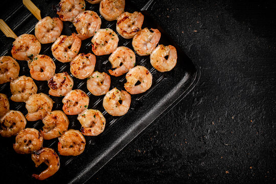 Shrimp on skewers are grilled in a grill pan. 