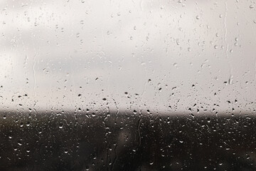 Raindrops on window background. Water droplets on glass surface. Rainy weather. Rain drops on background of gray clouds. Rainy day wallpaper
