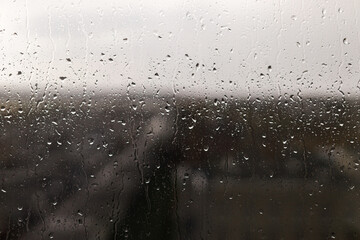 Raindrops on window background. Water droplets on glass surface. Rainy weather. Rain drops on background of gray clouds. Rainy day wallpaper