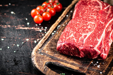 Raw beef on a cutting board with tomatoes.