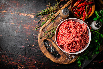 Fresh minced meat on a cutting board with parsley and chili pepper pods. 