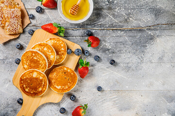 Homemade pancakes on a cutting board with honey and berries. 