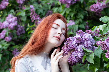 young girl with long red hair in the lilac flowers garden in spring