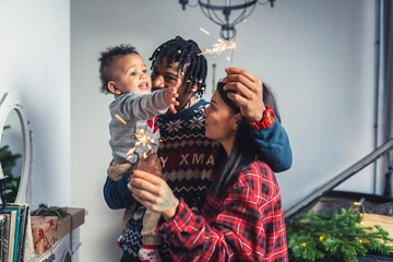 Smiling multicultural parents and their toddler with Christmas sparkling fire sticks. High quality photo