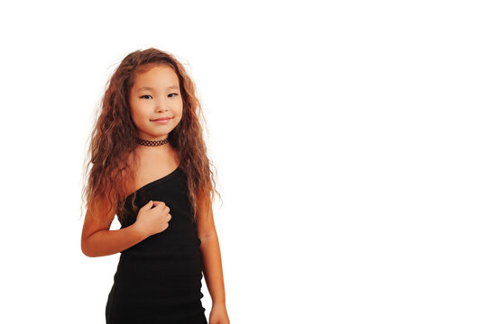 Smiling asian little girl with long curly hair posing at empty background, looking at camera. Studio shot stylish funny small fashionable model. Fashion education concept. Copy text space for ad