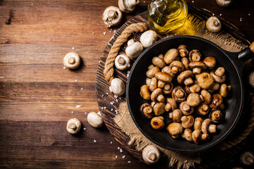 Frying pan with fried mushrooms on a wooden tray. 