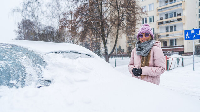 Woman in sunglasses standing next to the car burried under the snow . High quality photo