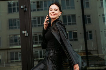Fototapeta premium Pretty brunette caucasian woman dressed leather suit with shoulder bag walking outside street hold mobile phone speaking. Businesswoman office CEO clerk. Smiling lady. Professional business owner