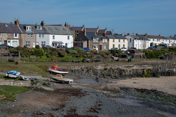 Boats in the rocky bay at fishing village Craster in Northumberland, UK. Against a backdrop of a...