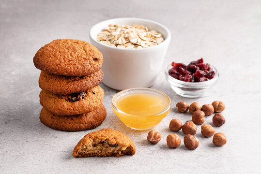 Blurred image of oatmeal cookies, honey in a plate, nuts, dried cranberries and oatmeal in the background.