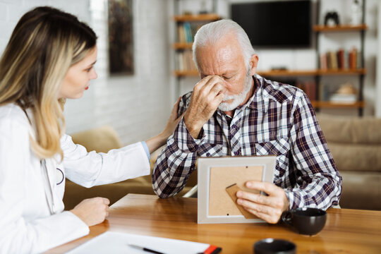 Female home caregiver comforting senior man who is talking about his old photo at home