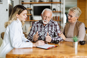Mature couple looking at their plan of care and medications with female nurse at home