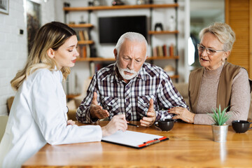 Mature couple looking at their plan of care and medications with female nurse at home