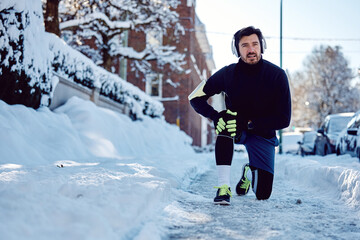 Athletic man holds his knee in pain while exercising on cold winter day.