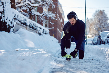 Fototapeta na wymiar Male athlete tying shoelace while working out outdoors in snow.