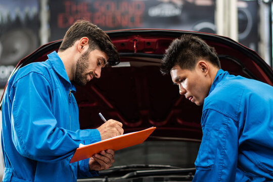 Auto mechanic checking maintenance checklist while colleague worker repair car at auto garage shop. After service for safety vehicle