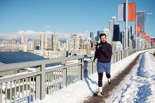 Athletic man with headphones jogging across bridge during winter.