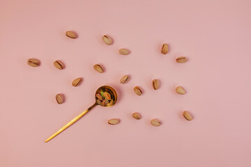 Pistachios in the spoon on the pink background, healthy nuts